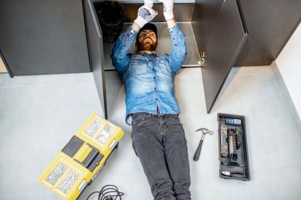 Man repairing kitchen plumbing Handyman repairing kitchen plumbing lying under the sink on the floor, view from above